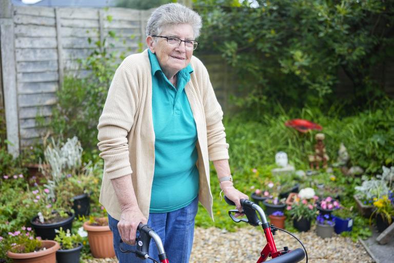 Older woman standing in her garden with a rollator