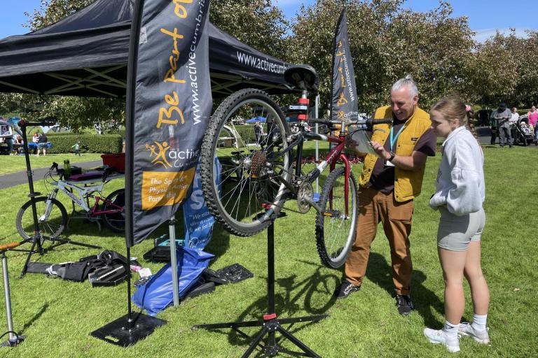 A man stood outdoors fixing a bike accompanied by a young female