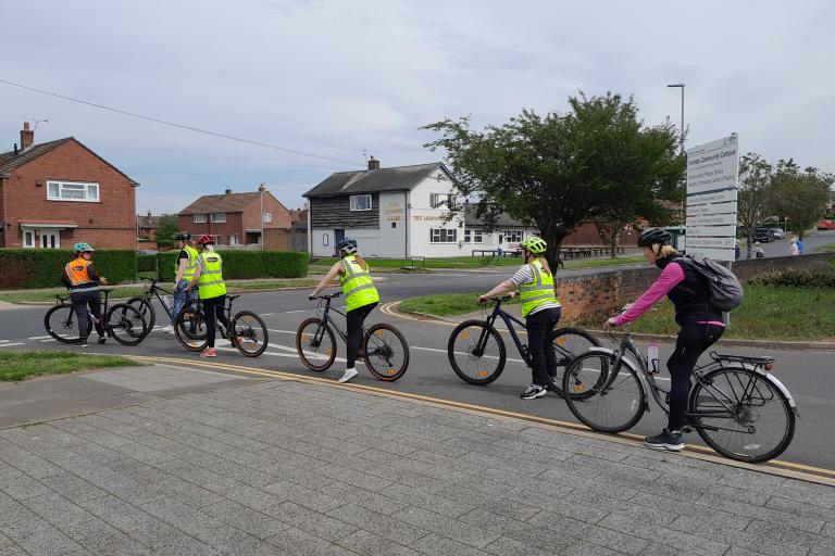 A group of mixed adults and children cycling on a road