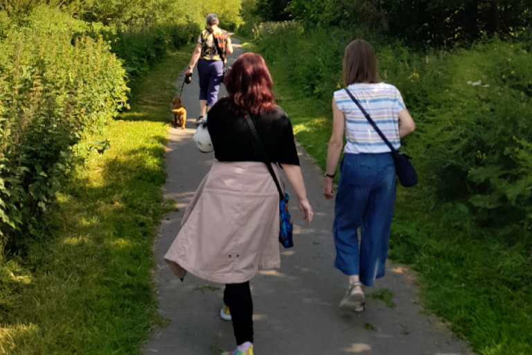 a group of ladies walking outdoors. One of them has a dog on a lead.