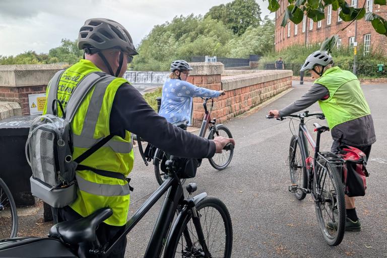 three cyclists stood on a cycle path holding bicycles