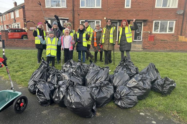 A group of men and women wearing high-vis jackets stood with a pile of filled black bin bags