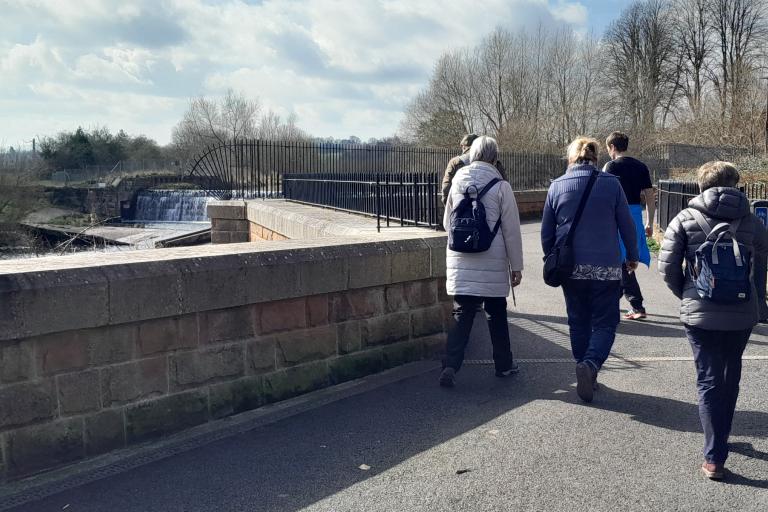 a group of adults walking outdoors along a river path