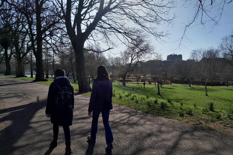 Two ladies walking outdoors in a park on a path lined with trees