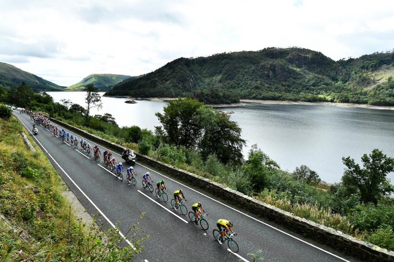 a group of cyclists racing on a road alongside a lake