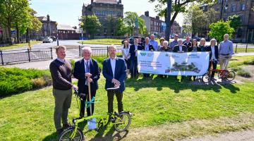 A group of people at Ramsden Square, Barrow standing with a spade, banner and bikes.