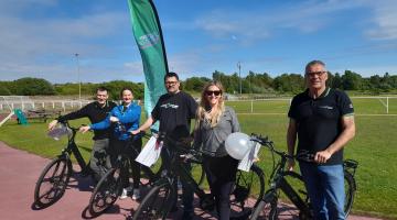 A group of adults stood outdoors next to e-bikes. They are smiling at the camera