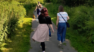 a group of ladies walking outdoors.  One of them has a dog on a lead.