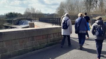 a group of adults walking outdoors along a river path