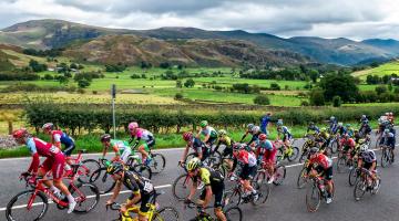 a group of cyclists taking part in a race with lake district fells in the background 