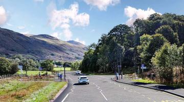 Artist's impression of the proposed signalised crossing on the A591 near Bridge End Farm. The image shows a new crossing with signal-controlled facilities, footways and waiting areas for walkers, wheelers, cyclists and horse riders, alongside bus stop infrastructure. Cars are travelling along the road, with woodland, fields and surrounding fells visible in the rural landscape.