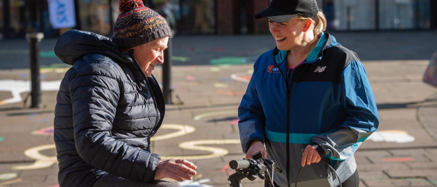 A person sitting on an electric bike assisted by a person from the Travel Actively team.