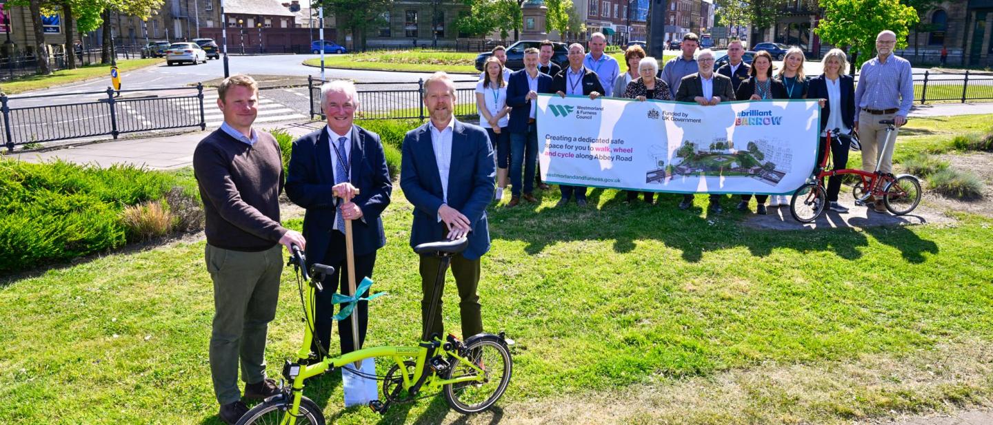 A group of people at Ramsden Square, Barrow standing with a spade, banner and bikes.